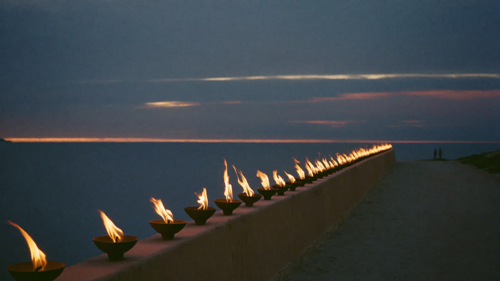 A long row of small clay lamps burning along a coastal wall at dusk.